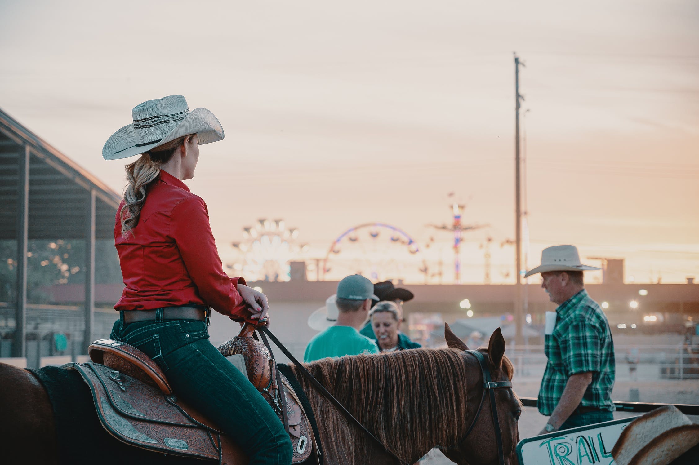 Girl riding horse at rodeo with carnival in the background.